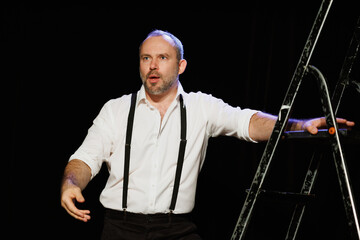 Shocked actor in shirt playing role near ladder on theater stage 