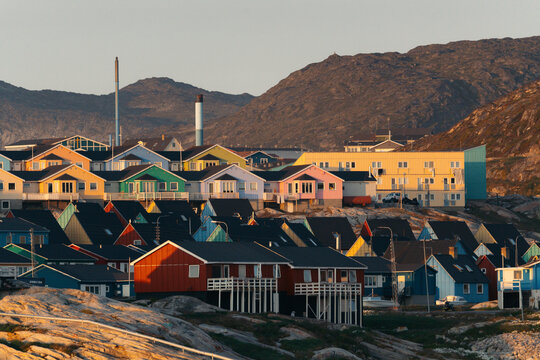 A vibrant cityscape of Ilulissat in Greenland glows under the surreal, golden hues of the midnight sun, casting an ethereal light over the colorful houses and coastal landscape