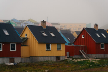 A vibrant cluster of traditional, colorful wooden houses dot the rugged, rocky hillsides of Ilulissat, Greenland