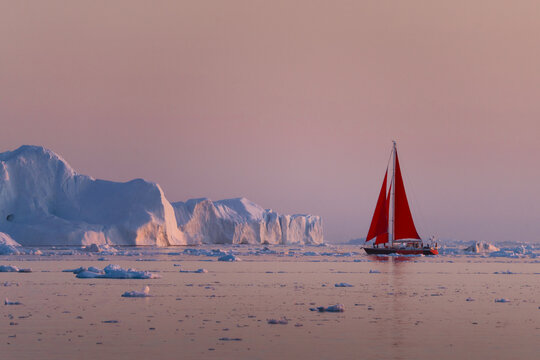 A solitary red sailboat courageously navigates through the surreal, glacial landscape of Greenland's Ilulissat Icefjord