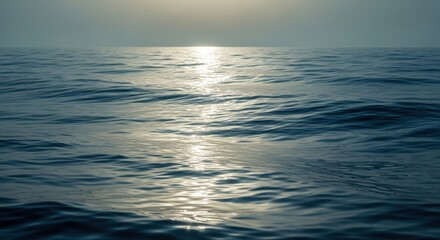 Obraz premium Calm ocean waves gently illuminated by the soft glow of the setting sun on the horizon.