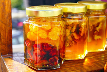 Jars of walnuts and raisins in honey on the sun. Concepts of natural preservation methods, sustainable local produce, zero-waste packaging, wholesome dessert alternative, and rustic home delicacies.