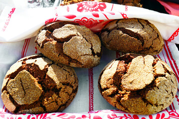 Four rustic dark rye bread loaves arranged on decorative embroidered kitchen towel. Symbol of traditional artisan sourdough baking, authentic bakery craftsmanship, and homemade whole grain bread. 