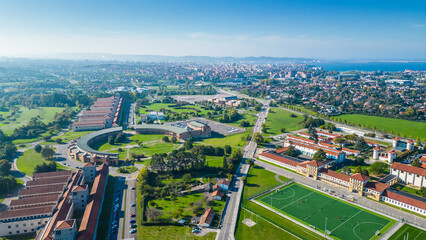 An impressive historic tower stands tall, offering a panoramic view of the vibrant coastal city of Gijon and its expansive bay under a clear blue sky.