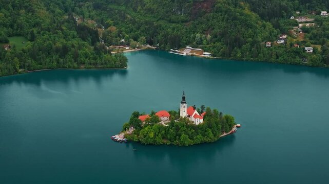 Aerial view of Church of the Assumption of Mary in the center of the lake Bled. Flying around small island on Bled Lake in Slovenia