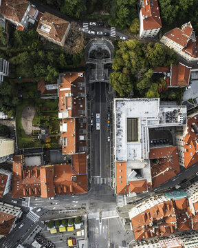 Aerial view of terracotta rooftops and lush green trees framing the bustling Via Galleria, leading towards a tunnel entrance, Trieste, Friuli-Venezia Giulia, Italy.