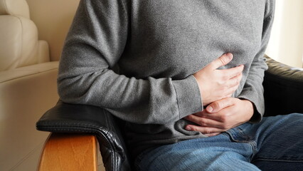 A man sitting in an armchair clutches his belly due to stomach ache