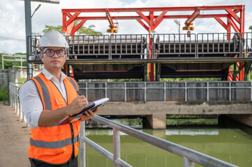 an engineer in safety vest inspects water gate structure, recording data on a sunny day