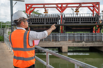 an engineer in safety vest inspects water gate structure, recording data on a sunny day