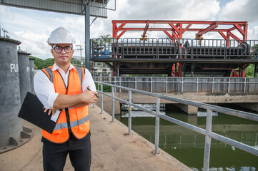 an engineer in safety vest inspects water gate structure, recording data on a sunny day