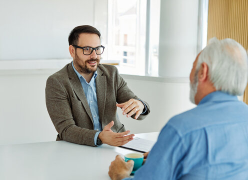 Two businessman having a meeting and lookung at a document or a contract agreement in the office, or a senior mad pensioner supported ny a real estate agent or advisor or a doctor. Teamwork and succes
