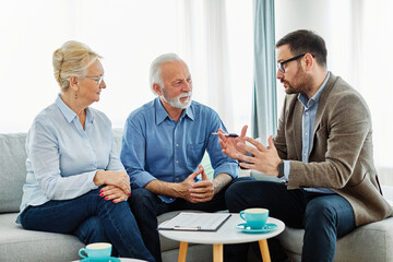 Portrait of a businessman or real estate agent or doctor shaking hands and signing a deal contract with senior couple in his office