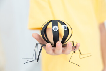 Black paper spider handmade by child for Halloween craft project, placed on bright background with festive mood and soft light, kids creativity, holiday decoration, and school art industry