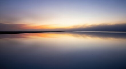 Obraz premium Tranquil sunset over a calm lake with a clear horizon and soft gradient sky reflecting warm orange and cool blue hues.