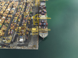 Trieste, Italy - 10 October 2025: Aerial view of the bustling port, where a colossal cargo ship meets a symphony of colorful containers under the watchful gaze of towering yellow cranes.