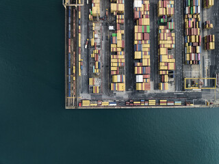 Trieste, Italy - 10 October 2025: Aerial view of a vibrant mosaic of stacked shipping containers at the port, contrasting with the deep turquoise waters of the Adriatic Sea.