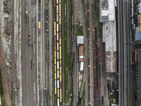 Trieste, Italy - 10 October 2025: Aerial view of a sprawling train yard, a tapestry of parallel tracks gleaming under the sky, framed by aged buildings and colorful train cars.