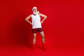 Festive Santa look man in red plaid shorts and hat poses happily against bright red studio...