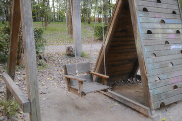 A swing hangs next to a wooden climbing structure in a Park during the day.