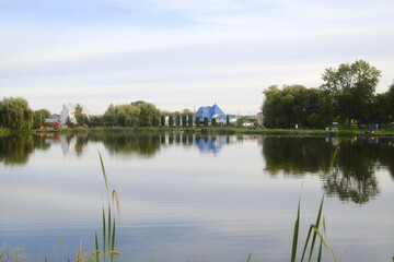 Obraz premium Calm water reflects the shoreline with buildings and trees on an overcast day.