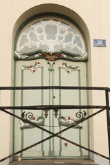 Wrought iron gate.Vintage green wooden door with white panels set in a rustic brick wall. A wreath with a purple ribbon decorates the entrance, and a pot of violet flowers adds charm 