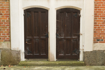 Old wooden door.Vintage green wooden door with white panels set in a rustic brick wall. A wreath with a purple ribbon decorates the entrance, and a pot of violet flowers adds charm
