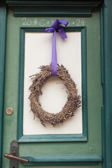 Classic countryside door with green and white panels framed by a red brick wall. A handmade wreath and a pot of purple flowers bring a cozy, welcoming atmosphere to this rustic entrance.