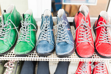 Colorful leather boots in green, blue, and red arranged in a row on a store display. Handmade craftsmanship, stylish design, and bright laces highlight their unique and modern character