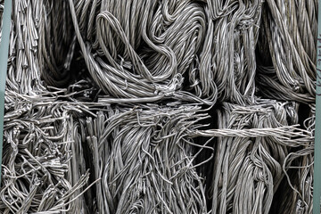 Neatly compacted stacks of tangled silver-colored metal wires bound with straps, ready for...