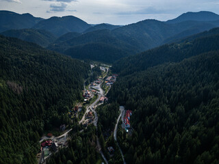 Aerial view of mountain valley village with road and river in conifer forest