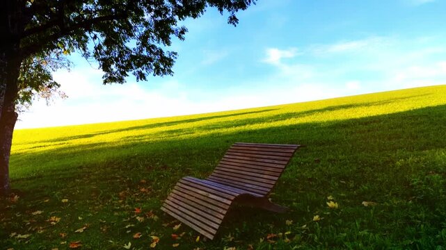 Gem&uuml;tliche Holzliege auf gr&uuml;ner Wiese im Schatten eines Baumes &ndash; perfekte Erholung und Entspannung im Garten, Natur genie&szlig;en, wohlf&uuml;hlen und relaxen in sommerlicher Naturidylle