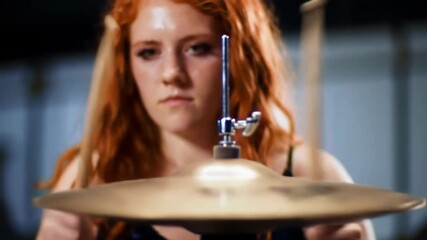 Ginger female drummer hitting cymbal in music studio, with blurred instruments, for music promotion