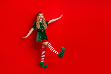 Festive elf dancer in green holiday costume posing joyfully on vibrant red background celebrating...
