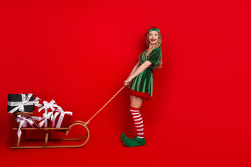 Festive female elf hauling a sleigh loaded with gifts against a vibrant red background embodying Christmas cheer