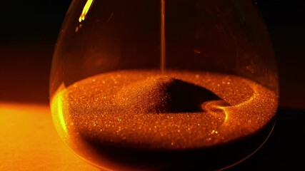 A video frame of an hourglass where golden sand flows, powerfully symbolizing the irreversible passing of time under dramatic, warm light.