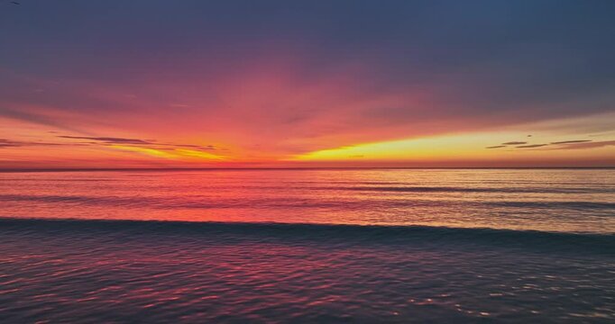 Vibrant Stunning Sea Sunset or See Sunrise Over Calm Ocean water At Dusk With Reflective Ripple surface of Red And Orange Waves