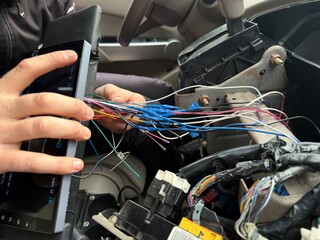 Car multimedia installation process with colorful electrical wires and dashboard disassembly. Close-up view of hands connecting cables during car audio system repair or upgrade