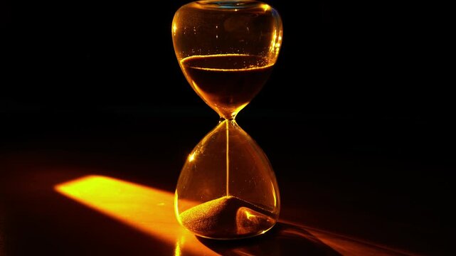 A video frame of an hourglass where golden sand flows, powerfully symbolizing the irreversible passing of time under dramatic, warm light.