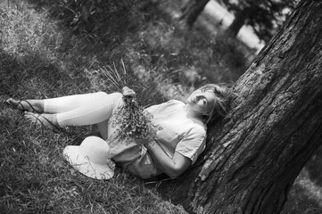 Fototapeta premium Woman resting under a tree while holding wildflowers in a peaceful outdoor setting during a sunny day