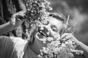 Woman smiling joyfully while holding flowers outdoors in bright light during a sunny day