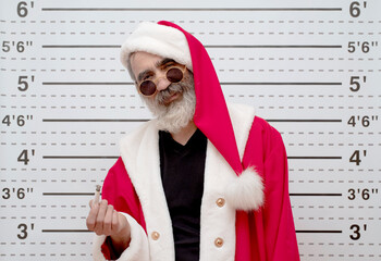Bad Santa Claus smoking a hand-rolled cigarette, Police Mugshot Board backdrop of a ruler with...