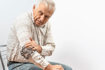 Arthritis symptoms, suffering from pain. The hands of the senior man massage a painful elbow. Chain symbolizing inflamed male joint, stiffness of movement. Old age, health. Close up view..