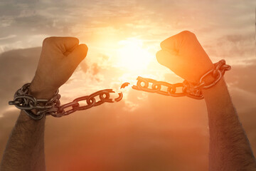 Men's hands breaking chains against the sky