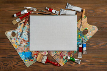 Stretched canvases with blank copy space, mock up. Old used brushes and palette knife in an artist's studio, palette with multi-colored spots of oil or acrylic paint, paint tubes.