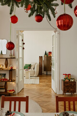 Elegant Christmas dining setup with red chairs, holiday tableware, and hanging evergreen branch with baubles.