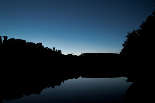 Wald nach Sonnenuntergang, der sich im See spiegelt.