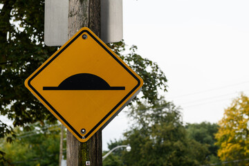 Yellow traffic warning sign cautioning drivers to slow down because the road contains a speed bump or speed hump ahead.