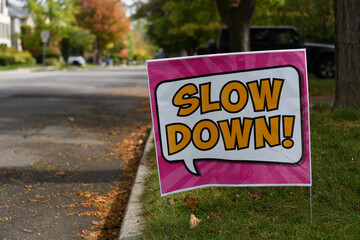 Sign planted in grass along a residential street asking drivers to slow down to minimize danger of passing vehicles.