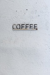 White, minimalist, textured stucco wall with a metal, raised letter sign advertising coffee.