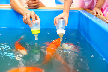 A child feeds vibrant koi fish using a bottle in a bright blue tank, capturing a tender moment of connection between humans and nature.